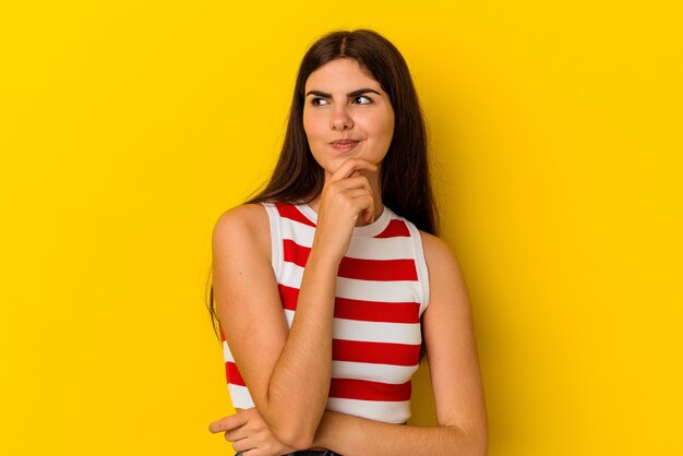 Jonge blanke vrouw geïsoleerd op gele muur denken en kijken, reflecterend zijn, nadenken, een fantasie hebben