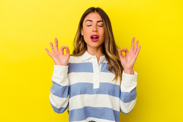 Jonge blanke vrouw geïsoleerd op gele muur ontspant na een zware werkdag, ze voert yoga uit.