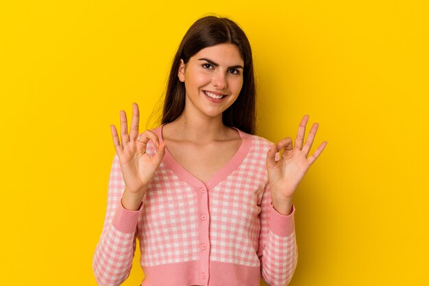 Jonge blanke vrouw geïsoleerd op gele muur vrolijk en zelfverzekerd tonend ok gebaar