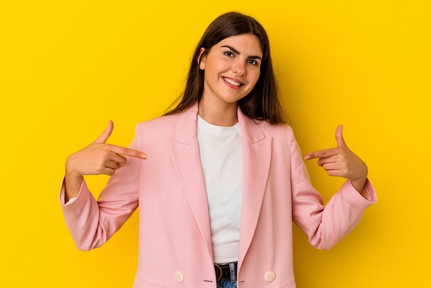 Jonge blanke vrouw geïsoleerd op gele muur wijst naar beneden met vingers, positief gevoel.