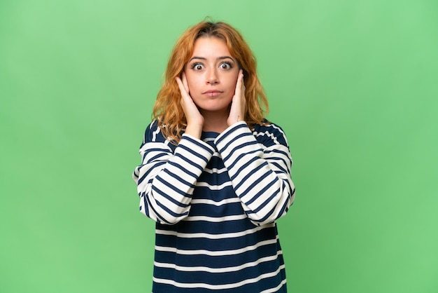 Jonge blanke vrouw geïsoleerd op groen scherm chroma sleutel achtergrond gefrustreerd en het bedekken van de oren