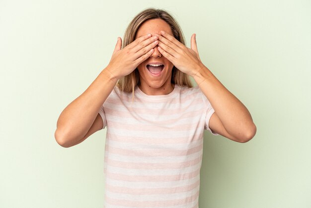 Jonge blanke vrouw geïsoleerd op groene achtergrond bedekt ogen met handen, glimlacht in grote lijnen wachtend op een verrassing.