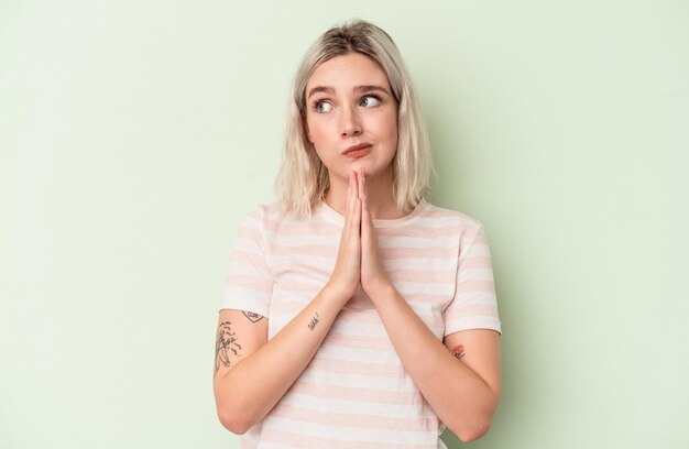 Foto jonge blanke vrouw geïsoleerd op groene achtergrond bidden, tonen toewijding, religieuze persoon op zoek naar goddelijke inspiratie.