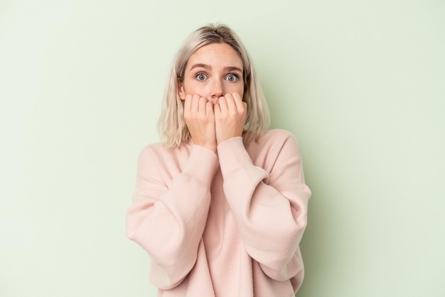 Jonge blanke vrouw geïsoleerd op groene achtergrond bijten vingernagels, nerveus en erg angstig.