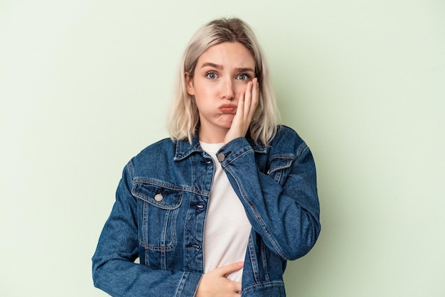 Jonge blanke vrouw geïsoleerd op groene achtergrond blaast wangen, heeft een vermoeide uitdrukking. Gezichtsuitdrukking concept.