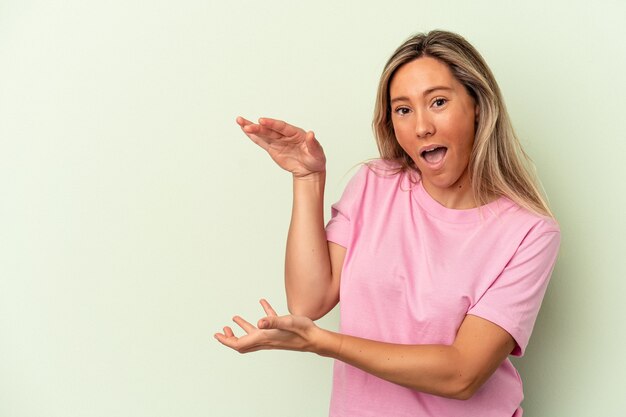 Jonge blanke vrouw geïsoleerd op groene achtergrond geschokt en verbaasd met een kopie ruimte tussen handen.