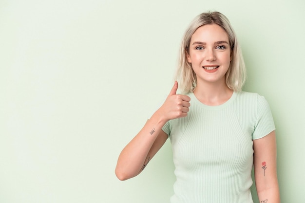 Jonge blanke vrouw geïsoleerd op groene achtergrond glimlachend en duim omhoog