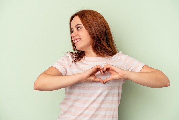 Jonge blanke vrouw geïsoleerd op groene achtergrond glimlachend en toont een hartvorm met handen.