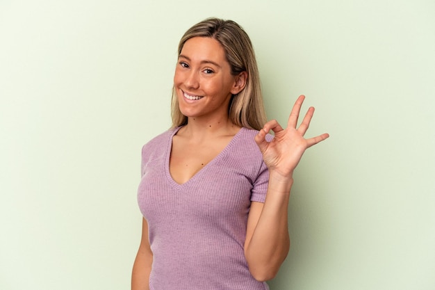 Jonge blanke vrouw geïsoleerd op groene achtergrond knipoogt en houdt een goed gebaar met de hand.