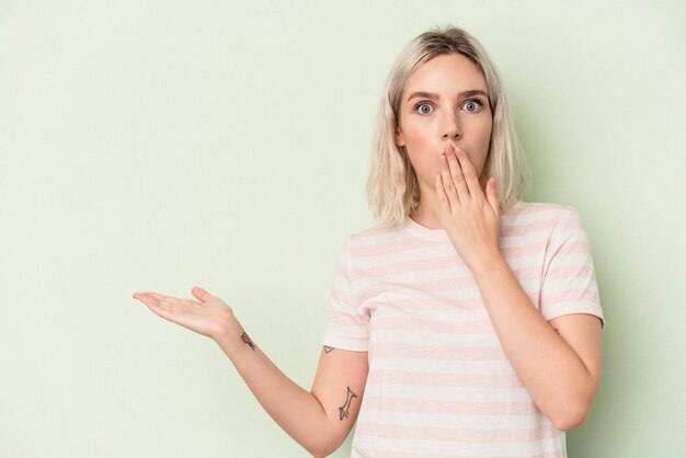 Jonge blanke vrouw geïsoleerd op groene achtergrond onder de indruk met kopie ruimte op palm.