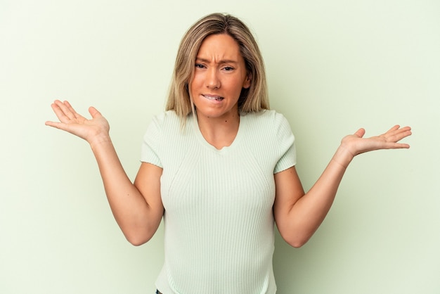 Jonge blanke vrouw geïsoleerd op groene achtergrond verward en twijfelachtig schouders ophalen om een kopie ruimte te houden.