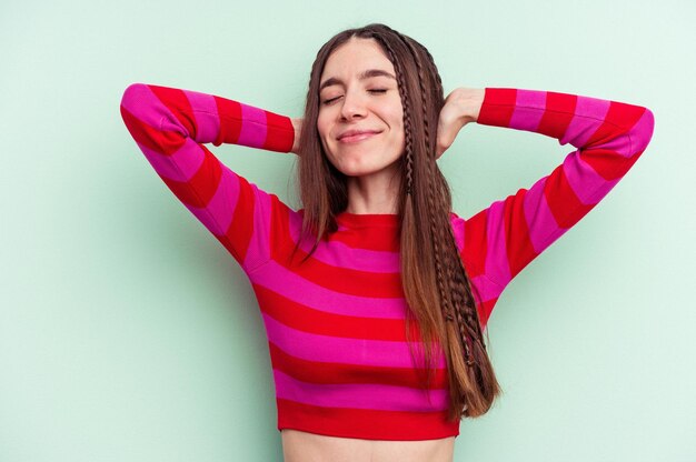 Jonge blanke vrouw geïsoleerd op groene achtergrond zelfverzekerd gevoel, met handen achter het hoofd.