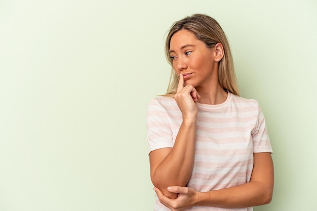 Jonge blanke vrouw geïsoleerd op groene achtergrond zijwaarts kijkend met twijfelachtige en sceptische uitdrukking.