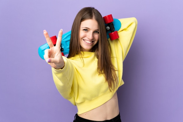 Jonge blanke vrouw geïsoleerd op paars met een skate overwinning gebaar doen