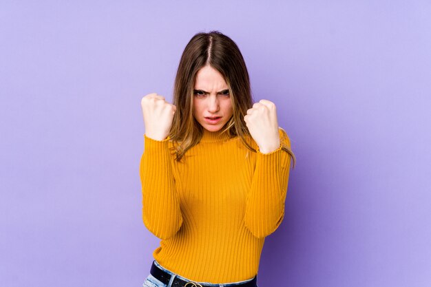 Jonge blanke vrouw geïsoleerd op paars met vuist, agressieve gezichtsuitdrukking.