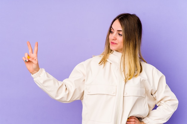 Jonge blanke vrouw geïsoleerd op paarse achtergrond vrolijk en zorgeloos met een vredessymbool met vingers.