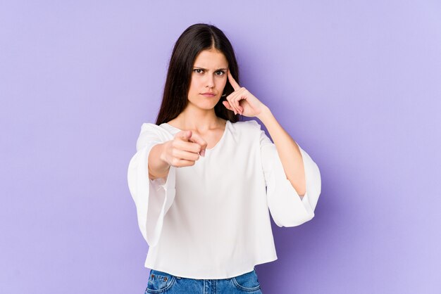 Jonge blanke vrouw geïsoleerd op paarse muur wijzende tempel met vinger, denken, gericht op een taak.