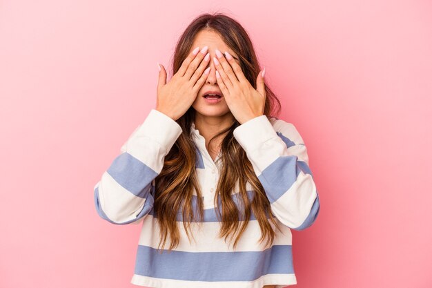 Jonge blanke vrouw geïsoleerd op roze achtergrond bang voor ogen met handen.