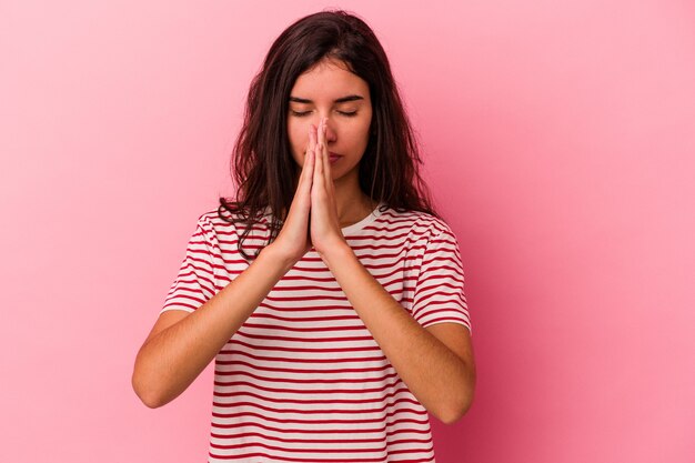 Jonge blanke vrouw geïsoleerd op roze achtergrond bidden, tonen toewijding, religieuze persoon op zoek naar goddelijke inspiratie.