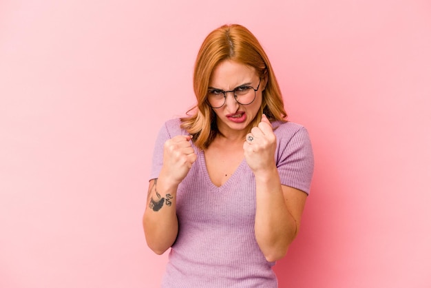 Jonge blanke vrouw geïsoleerd op roze achtergrond boos schreeuwen met gespannen handen.