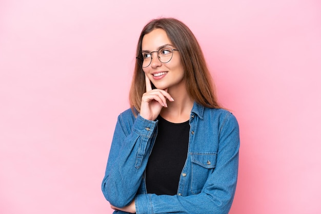 Jonge blanke vrouw geïsoleerd op roze achtergrond denkt aan een idee terwijl ze omhoog kijkt