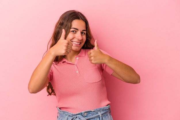 Jonge blanke vrouw geïsoleerd op roze achtergrond die beide duimen opheft, glimlachend en zelfverzekerd.