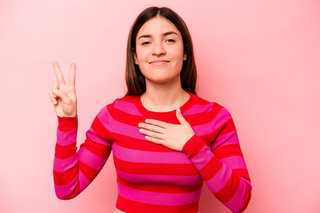 Jonge blanke vrouw geïsoleerd op roze achtergrond die een eed aflegt en hand op de borst legt