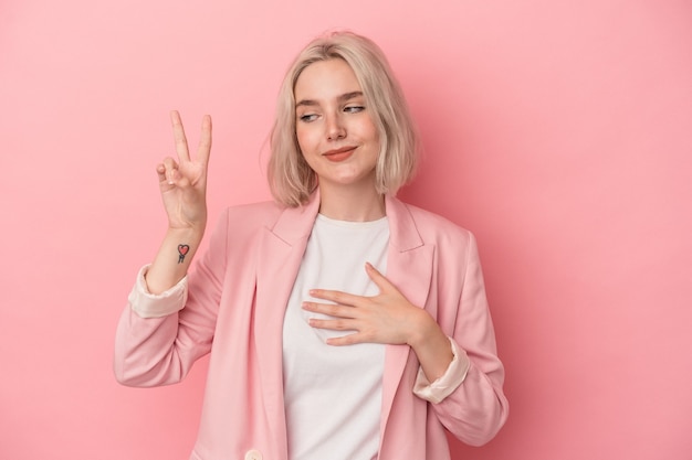 Jonge blanke vrouw geïsoleerd op roze achtergrond die een eed aflegt, hand op de borst.