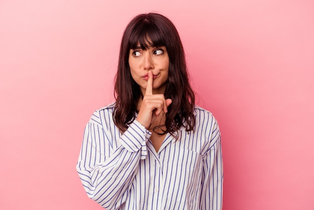 Jonge blanke vrouw geïsoleerd op roze achtergrond die een geheim houdt of om stilte vraagt.