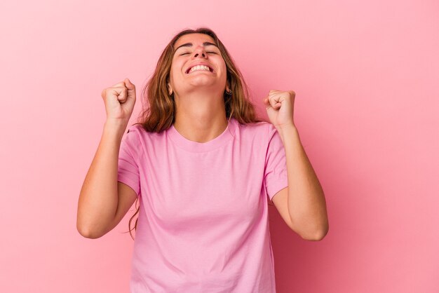 Jonge blanke vrouw geïsoleerd op roze achtergrond die een overwinning, passie en enthousiasme, gelukkige uitdrukking viert.