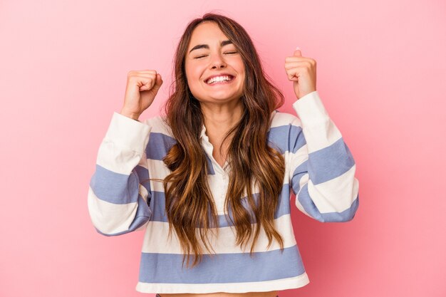 Jonge blanke vrouw geïsoleerd op roze achtergrond die een overwinning, passie en enthousiasme, gelukkige uitdrukking viert.