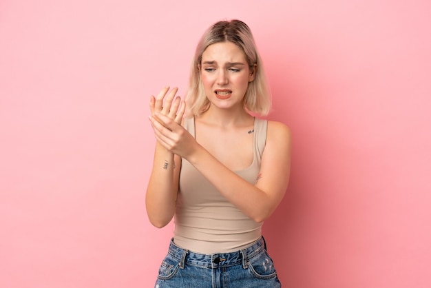 Jonge blanke vrouw geïsoleerd op roze achtergrond die lijdt aan pijn in handen