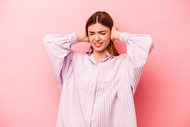 Jonge blanke vrouw geïsoleerd op roze achtergrond die oren bedekt met handen