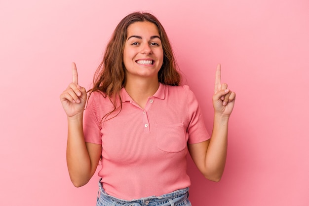 Jonge blanke vrouw geïsoleerd op roze achtergrond geeft aan dat met beide voorvingers een lege ruimte wordt weergegeven.