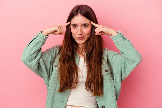 Jonge blanke vrouw geïsoleerd op roze achtergrond gericht op een taak, wijsvingers wijzend hoofd houden.