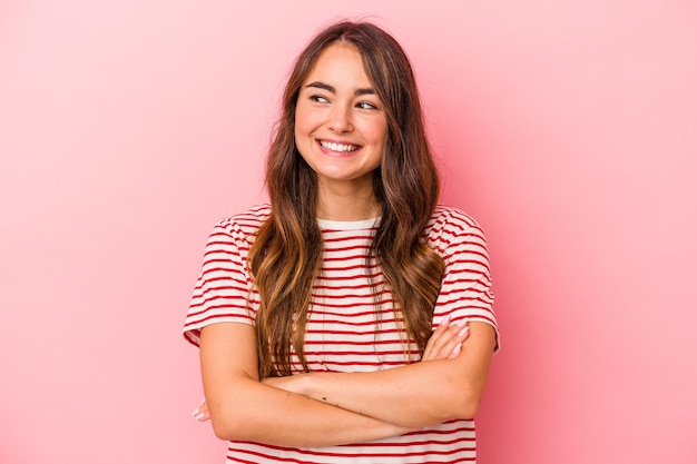 Jonge blanke vrouw geïsoleerd op roze achtergrond glimlachend zelfverzekerd met gekruiste armen.