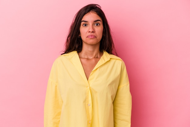 Jonge blanke vrouw geïsoleerd op roze achtergrond haalt schouders op en verwarde ogen.