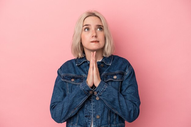 Jonge blanke vrouw geïsoleerd op roze achtergrond hand in hand bidden in de buurt van mond, voelt zich zelfverzekerd.