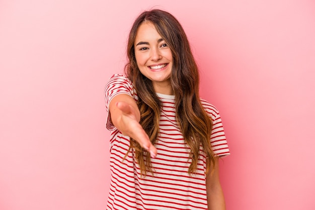 Jonge blanke vrouw geïsoleerd op roze achtergrond hand uitrekken op camera in begroeting gebaar.