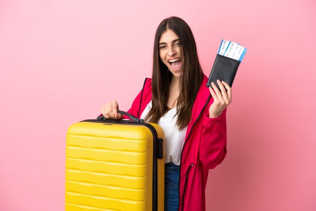 Jonge blanke vrouw geïsoleerd op roze achtergrond in vakantie met koffer en paspoort