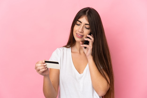 Jonge blanke vrouw geïsoleerd op roze achtergrond kopen met de mobiele telefoon met een creditcard