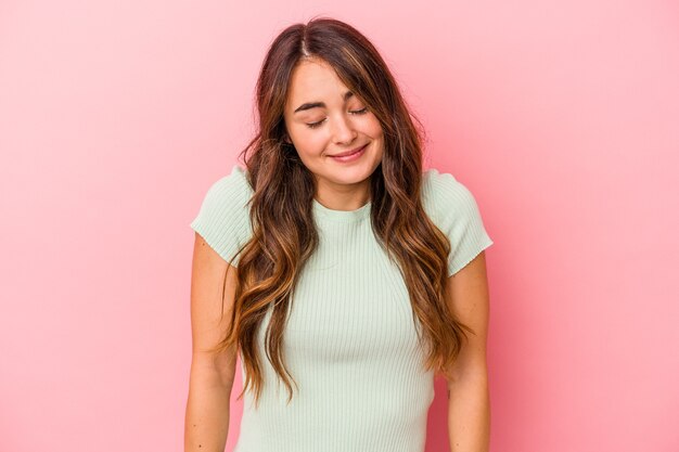 Jonge blanke vrouw geïsoleerd op roze achtergrond lacht en sluit de ogen, voelt zich ontspannen en gelukkig.