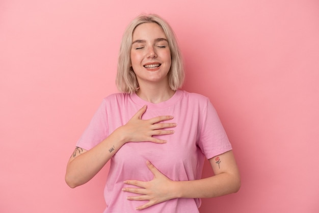 Jonge blanke vrouw geïsoleerd op roze achtergrond lacht vrolijk en heeft plezier met het houden van handen op de maag.