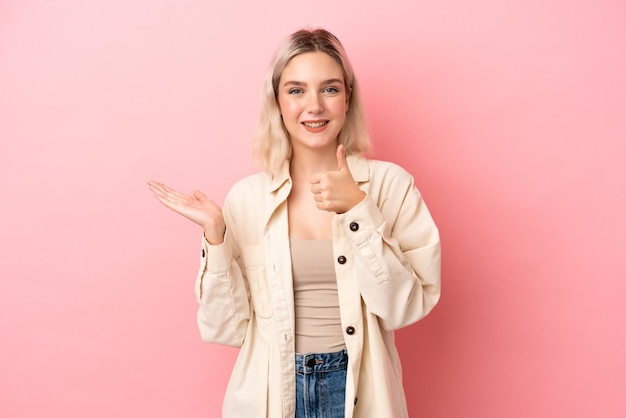 Jonge blanke vrouw geïsoleerd op roze achtergrond met copyspace denkbeeldig op de palm om een advertentie in te voegen en met duimen omhoog