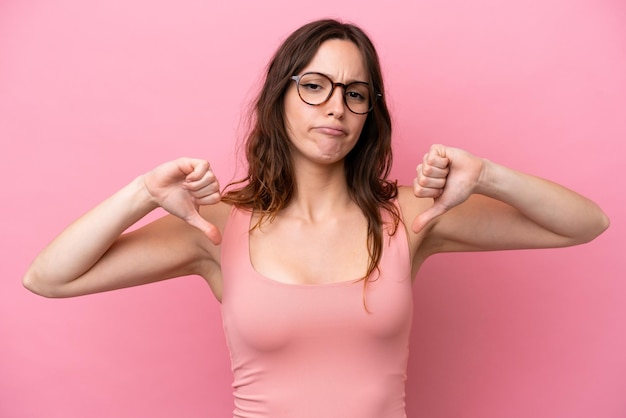 Foto jonge blanke vrouw geïsoleerd op roze achtergrond met duim omlaag met twee handen