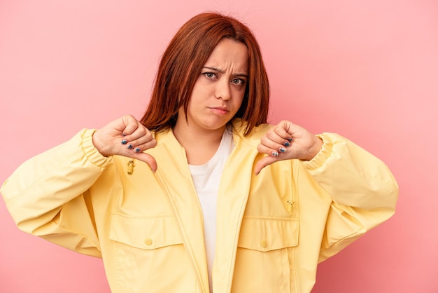 Jonge blanke vrouw geïsoleerd op roze achtergrond met duim omlaag, teleurstelling concept.