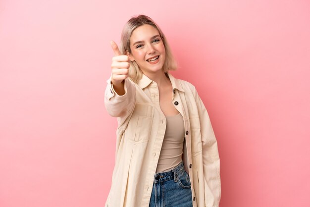 Jonge blanke vrouw geïsoleerd op roze achtergrond met duimen omhoog omdat er iets goeds is gebeurd