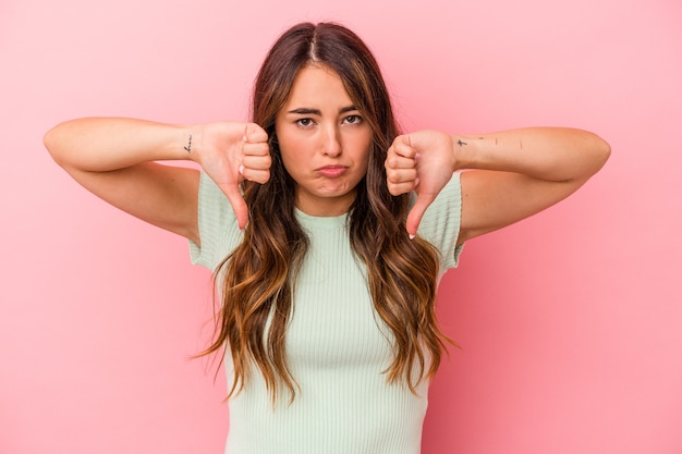 Jonge blanke vrouw geïsoleerd op roze achtergrond met een afkeer gebaar, duim omlaag. Onenigheid begrip.