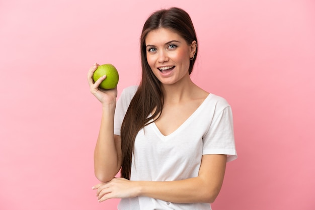 Jonge blanke vrouw geïsoleerd op roze achtergrond met een appel en happy
