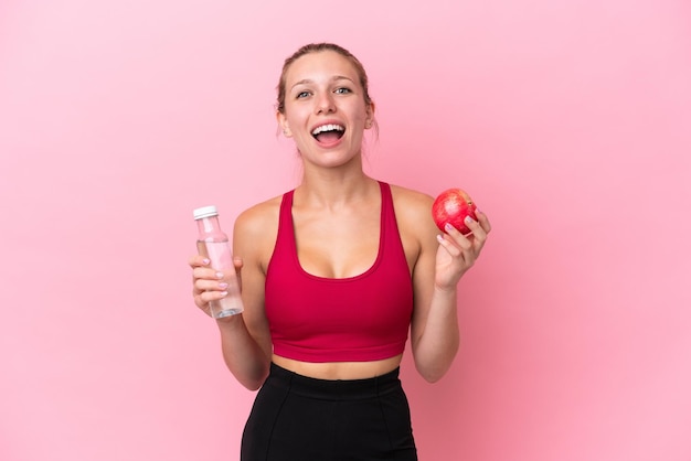 Jonge blanke vrouw geïsoleerd op roze achtergrond met een appel en met een fles water